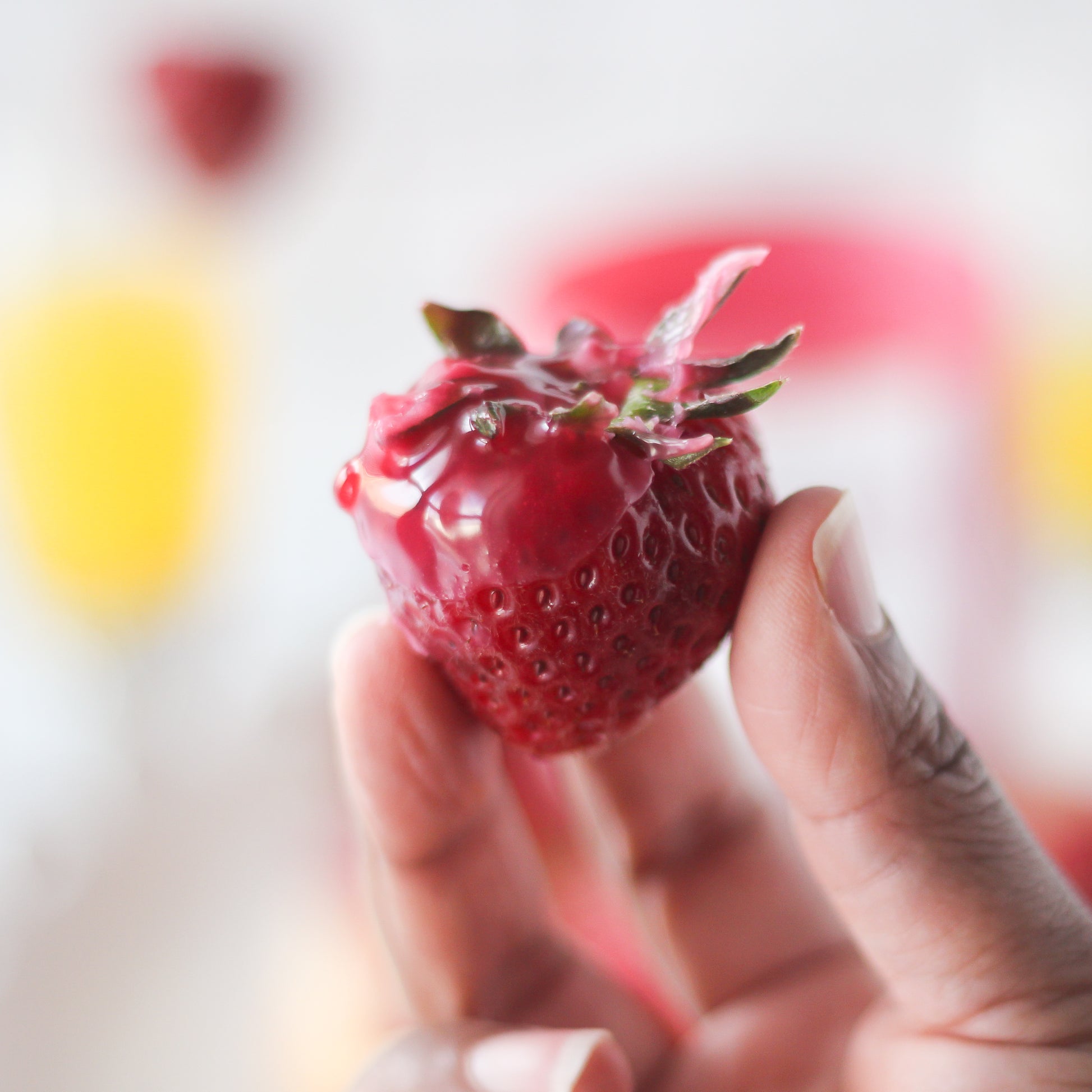 Hand holding a strawberry with a blurred colorful background