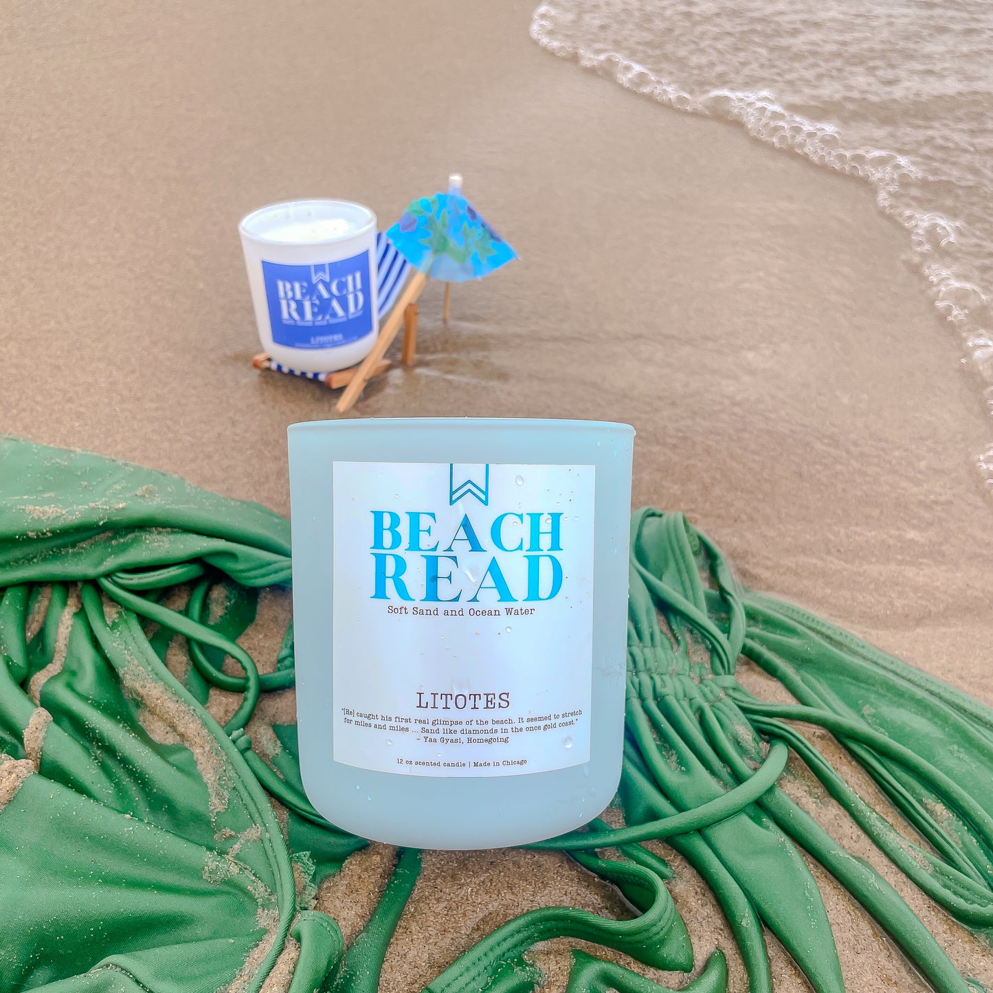 Candle labeled 'Beach Read' on a sandy beach with a small umbrella and towel.