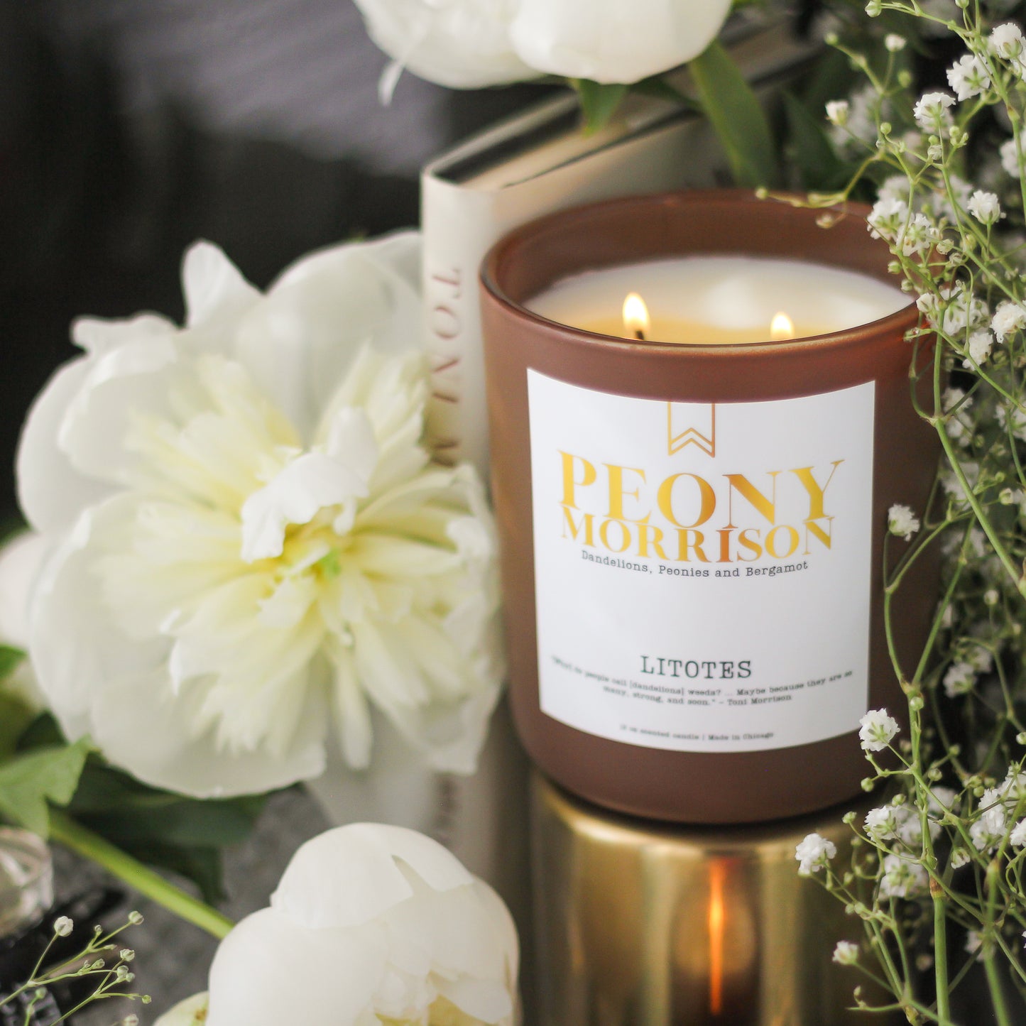 Candle with 'Peony Morrison' label surrounded by white flowers