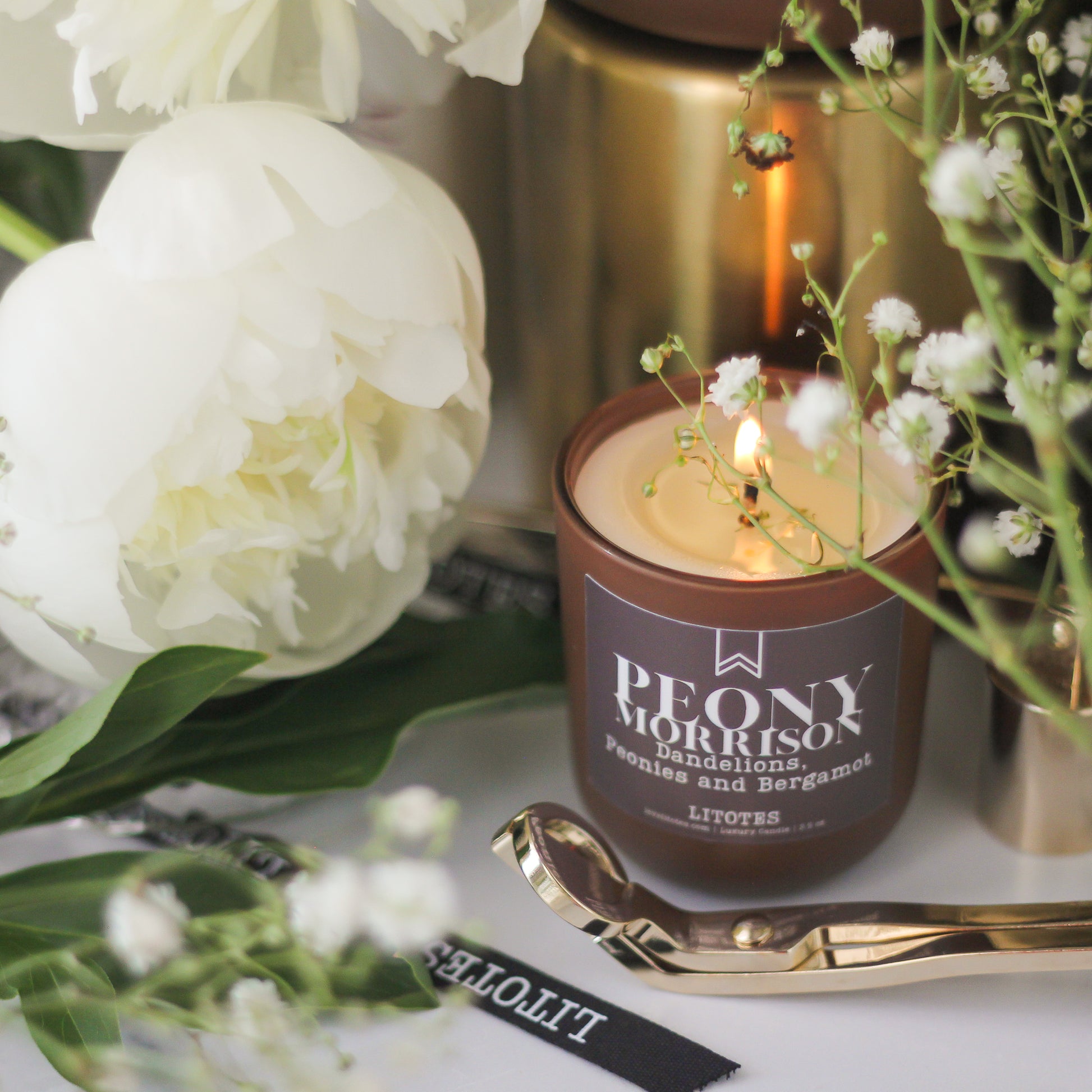 Lit candle in a decorative container with flowers and a gold spoon on a white surface